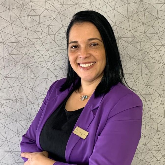 Gerente Diana de terninho roxo e bracos cruzados sorrindo para foto