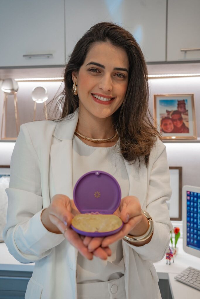 Doutora Maisa vestida de branco segurando os alinhadores ortodonticos Invisalign dentro de uma caixinha roxa com as maos