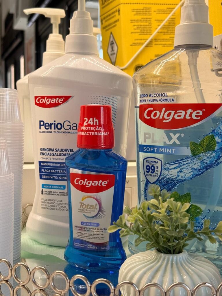 Três enxaguantes bucais da marca Colgate, sendo os dois da direita da foto de cor azul e garrafa transparente e o Periogard da esquerda em garrafa branca fosca