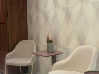 Recepção da clinica, composta por 2 poltronas brancas com uma mesinha entre elas e uma cestinha com pro pé no chao