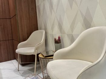 Recepção da clinica, composta por 2 poltronas brancas com uma mesinha entre elas e uma cestinha com pro pé no chao